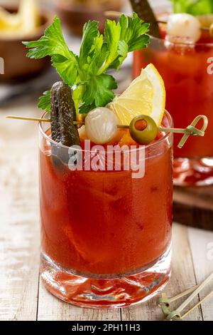 Cocktail Bloody mary garni de céleri, citron, cornichon, oignon et olive sur une table en bois Banque D'Images