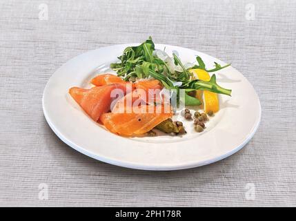 Carpaccio de saumon avec arugula, citron, concombre mariné et câpres sur plaque blanche Banque D'Images