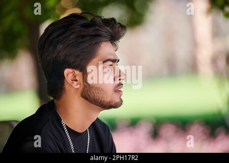Beau portrait de jeune indien en t-shirt noir et chaîne de cou argent sur fond de parc vert extérieur, gros plan portrait de mâle hindou. Beau moi Banque D'Images