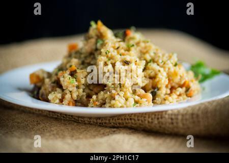 boulgour cuit avec des légumes, des carottes et des champignons séchés dans une assiette sur une table en bois. Banque D'Images