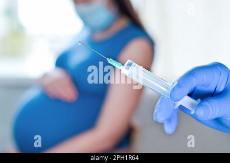 Vaccination des femmes enceintes. Femme enceinte au visage masque se faire vacciner en clinique. Médecin donnant Corona virus vaccin injection patient. Grippe Covid-19 Pro Banque D'Images