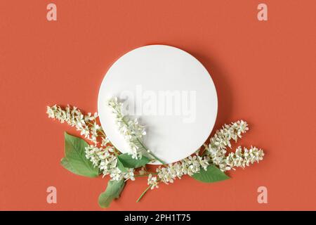 Podium pour la présentation des produits. Résumé forme géométrique minimale sur fond rouge orange. Une forme de pierre, fleurs blanches, ombre molle. Scène, Showca Banque D'Images