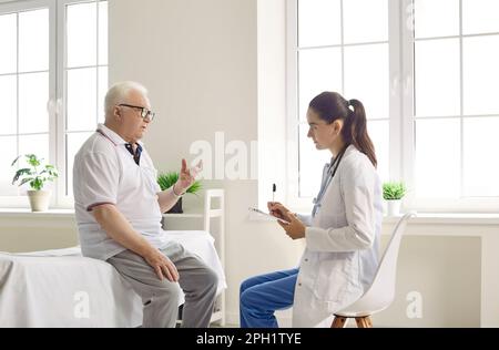 Un homme âgé parle de son état de santé à son médecin qui prend des notes sur le presse-papiers. Banque D'Images