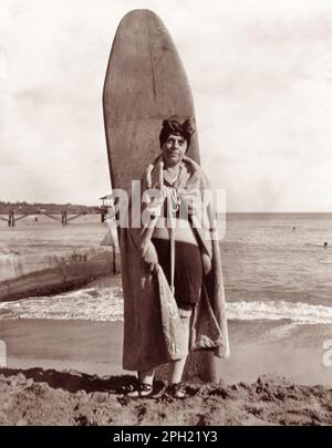 Portrait vintage d'une femme touriste senior posant avec une planche de surf en bois sur la plage de Waikiki à Honolulu, Hawaï, dans le 1920s. Banque D'Images