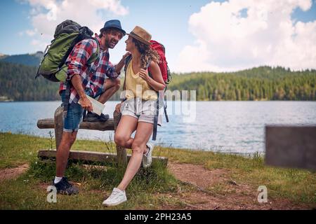 Un jeune couple bavarde en faisant une pause au lac pendant la randonnée dans la montagne par une belle journée. Voyage, nature, randonnée Banque D'Images