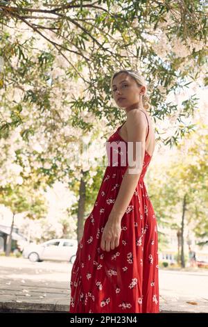 Femme blonde vêtue d'une robe ondulée rouge devant l'arbre. Mode, élégance, concept de style de vie. Banque D'Images