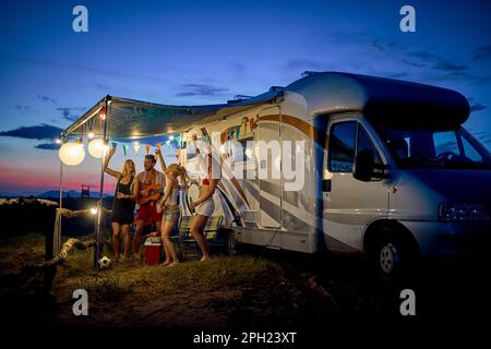 Amusez-vous avec des amis au camp, devant le camping-car. Jeune groupe de personnes dansant, jouant de la guitare, et célébrant. L'été. Voyage, week-end, li Banque D'Images