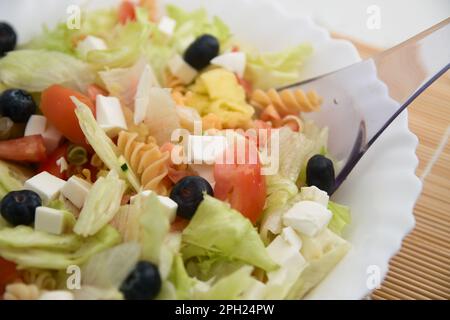 Salade fraîche avec laitue, tomate, concombres, canneberges, fromage et pâtes dans un cadre d'été lumineux Banque D'Images