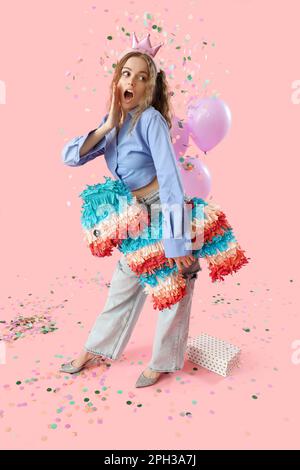 Surprise jeune femme avec pinata célébrant l'anniversaire sur fond rose Banque D'Images