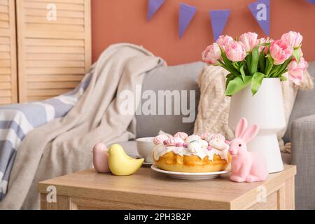 Gâteau de Pâques, lapin, cailles en porcelaine et vase avec fleurs de tulipe sur table dans le salon Banque D'Images