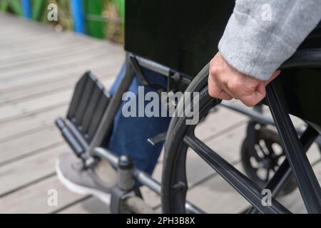 Femme méconnue se promenant dans un fauteuil roulant, à l'extérieur. Gros plan d'une main de femme en déplaçant le fauteuil roulant vers l'avant. Banque D'Images