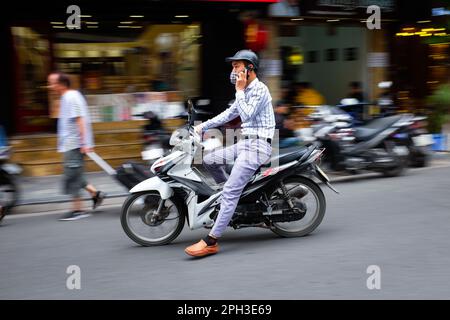 Un jeune homme en mobylette prend un appel téléphonique à Hanoi, Vietnam, en 2023. Banque D'Images