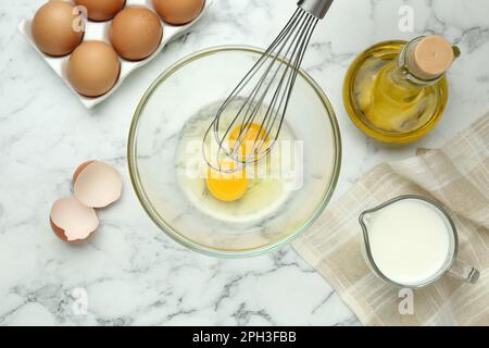 Fouettez les œufs dans un bol près des autres ingrédients sur une table en marbre blanc, posez-les à plat Banque D'Images