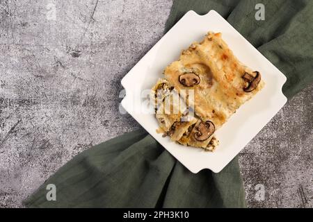 Cannelloni farcies à la viande et au fromage cuits dans une sauce au béchamel sur une assiette carrée sur fond gris foncé. Vue de dessus, plan d'agencement Banque D'Images