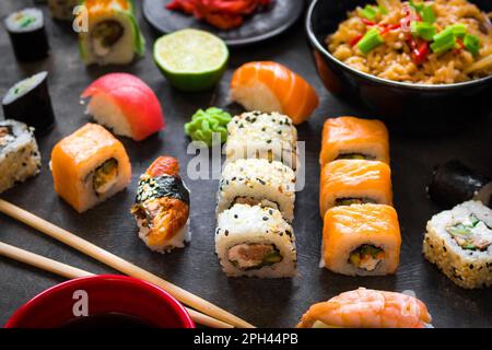 Table servie avec des sushis et de la cuisine japonaise traditionnelle sur fond sombre. Petits pains à sushi, wakame hiyashi, soupe miso, ramen, riz frit aux légumes Banque D'Images