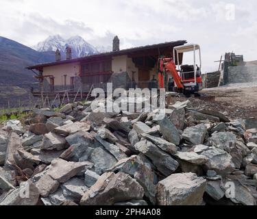 Les Grange ferme à nus dans la vallée d'Aoste Italie avec de grands morceaux de pierre en face et un creuseur. Des montagnes enneigées derrière Banque D'Images