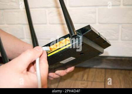 Routeur WiFi, à l'arrière du routeur, tenant le routeur à la main avec des fils Banque D'Images