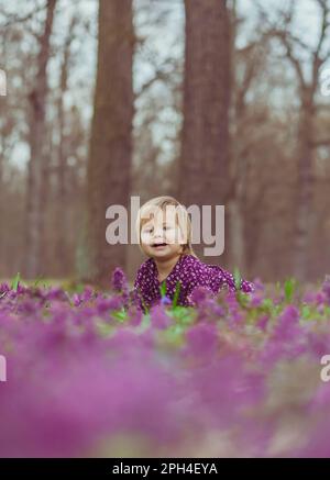 bébé blond dans une robe colorée se trouve dans une forêt de la glade de fleurs Banque D'Images