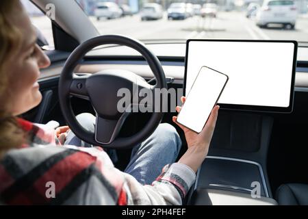 Une femme pilote dans une voiture tient un smartphone avec un écran blanc. Photo de haute qualité Banque D'Images