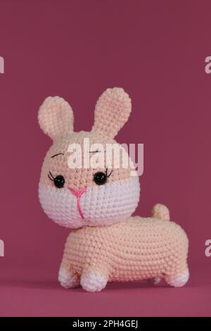 Symbole du concept de Pâques catholique. Rose mignon lapin de Pâques crocheté, art fait à la main Poupée de lapin Amigurumi sur fond rose. Jouet bricolage doux fait de cott Banque D'Images