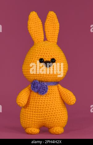 Lapin orange de Pâques avec noeud papillon violet, crocheté, art fait à la main Poupée de lapin Amigurumi sur fond rose. Jouet bricolage doux en coton et laine. Symbo Banque D'Images