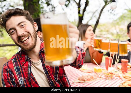 Un homme caucasien se tient à l'avant-garde, élevant un grand stein de bière. Le groupe, applaudit et trinque leurs lunettes ensemble. Banque D'Images
