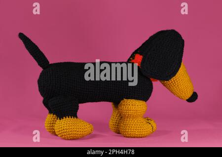 Un dachshund noir et rouge crochetté de laine naturelle et de coton, art fait à la main Vue latérale. Poupée de chien Amigurumi sur fond rose. Un jouet à faire soi-même fou Banque D'Images