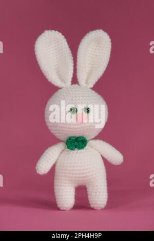 Symbole du concept de Pâques catholique. Lapin blanc de Pâques crocheté, art fait à la main Poupée de lapin Amigurumi sur fond rose. Vue avant. Banque D'Images