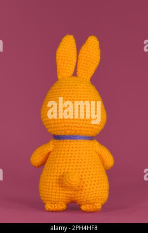 Lapin orange de Pâques avec noeud papillon violet, crocheté, art fait à la main Poupée de lapin Amigurumi sur fond rose. Jouet bricolage doux en coton et laine. Symbo Banque D'Images