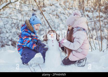 garçon et fille sculptent le bonhomme de neige dans le parc d'hiver Banque D'Images