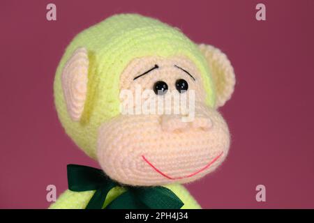 Jouet bricolage doux en coton naturel et laine. Joli petit singe avec noeud sur le cou crocheté, art fait à la main Amigurumi un singe vert avec de grandes oreilles Banque D'Images