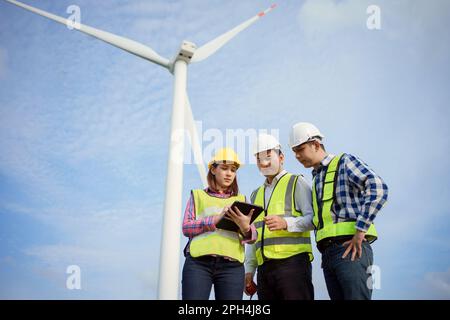 Une équipe d'ingénieurs asiatiques discutant et vérifiant les éoliennes d'une ferme éolienne. Technologie des énergies renouvelables et durabilité. Banque D'Images