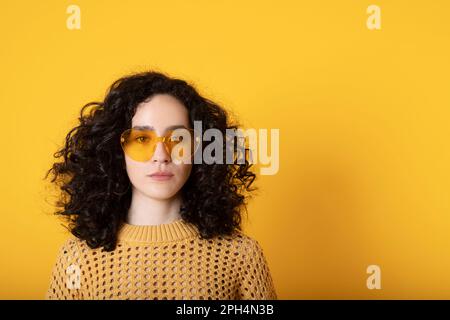 Fille à cheveux noirs bouclés avec des lunettes tendance en forme de coeur Banque D'Images