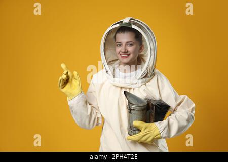 Apiculteur en uniforme avec un pot de fumée pointant vers quelque chose sur fond jaune Banque D'Images