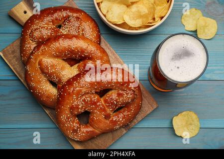 Bretzels frais savoureux, chips de pommes de terre et verre de bière sur une table en bois bleu clair, plat Banque D'Images