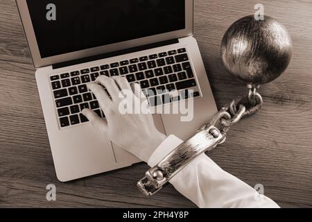 Vue de dessus d'une femme avec balle et chaîne sur sa main en utilisant un ordinateur portable sur une table en bois, effet sépia. Dépendance à l'Internet Banque D'Images