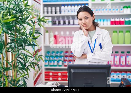 Une jeune femme hispanique travaillant dans une pharmacie pense être fatiguée et ennuie avec des problèmes de dépression avec des bras croisés. Banque D'Images