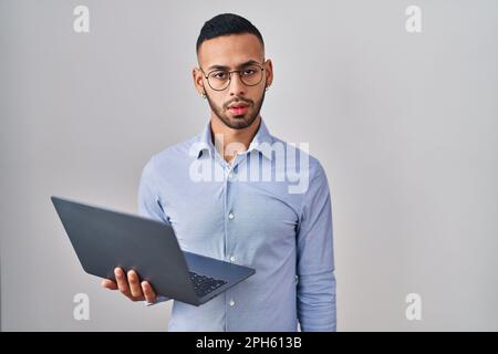 Jeune homme hispanique qui travaille avec un ordinateur portable a l'air endormi et fatigué, épuisé pour la fatigue et le pendu, les yeux paresseux le matin. Banque D'Images
