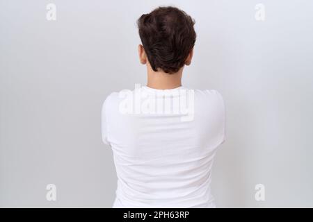 Jeune homme non binaire portant un t-shirt blanc décontracté debout en arrière regardant loin avec les bras croisés Banque D'Images