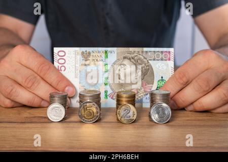 Un billet de 500 zlotys tenu par un homme devant lui, des piles de pièces polonaises devant, le concept d'épargne et de multiplication de l'argent, la monnaie polonaise Banque D'Images