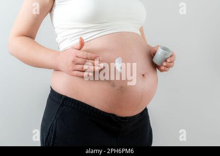 Femme enceinte appliquant de la crème blanche sur le ventre avec des ecchymoses par injections prenant soin de la peau Banque D'Images