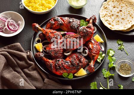 Poulet tandoori de style indien sur plaque sur fond de pierre sombre. Cuisses de poulet marinées au yaourt et aux épices. Vue rapprochée Banque D'Images