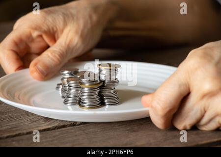 une pile de pièces de monnaie sur une assiette blanche sur une ancienne table en bois et de vieilles mains de femmes ont versé une assiette à la maison dans la cuisine Banque D'Images