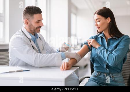 Jeune femme européenne se vaccine contre le coronavirus, homme d'âge moyen médecin faisant une injection dans l'épaule femelle Banque D'Images