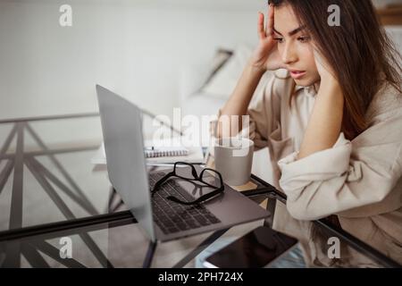 Fatigué malheureux millénaires race mixte regard de femme portable, souffrant de travail excessif, de pression et de maux de tête Banque D'Images