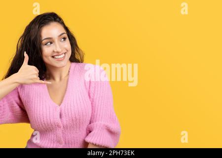 Bonne jeune caucasienne brune femme montrant le signe de téléphone avec la main, regardez l'espace libre Banque D'Images