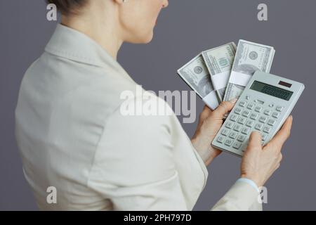 Gros plan sur une femme employée dans un costume d'affaires léger avec calculatrice et dollars packs d'argent sur fond gris. Banque D'Images