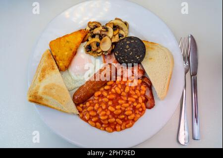 Tableau blanc avec petit déjeuner anglais complet avec bacon, œuf frit, haricots, tomate, saucisse rôtie, pudding noir, fons, pommes de terre sautées et champignons frits c Banque D'Images