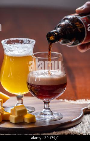 Verres de bière blonde jaune belge et brune foncée fabriqués en abbaye et en bois avec une variété de fromages belges, plats et bières assortis en Belgique Banque D'Images