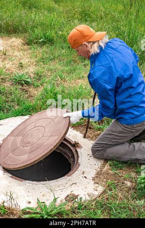 l'homme a ouvert le couvercle de l'orifice d'égout pour pomper les eaux usées. Banque D'Images